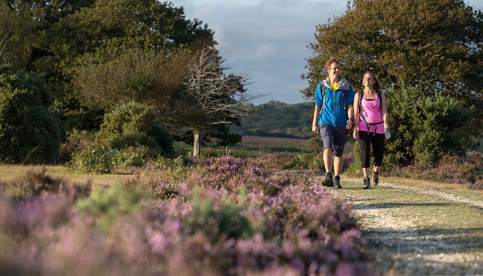 A man and woman hiking in the New Forest, Hampshire, surrounded by blooming greenery.